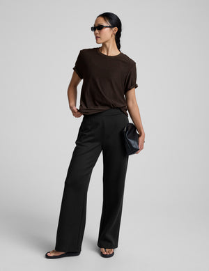 model wearing a brown t-shirt and pants on a light gray background. 