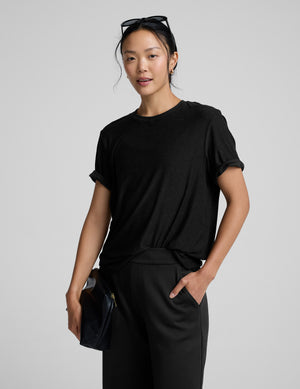 Person wearing a black t-shirt and black pants on a gray background. 