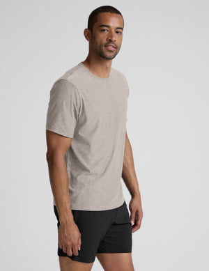 Man wearing a beige t-shirt and black shorts against a plain background. 