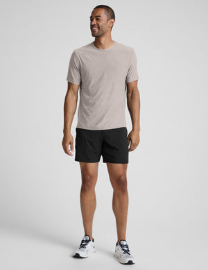 Man wearing a beige t-shirt and black shorts against a plain background. 