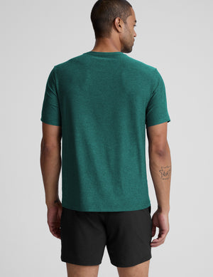 Man wearing a green t-shirt and black shorts on a light gray background. 