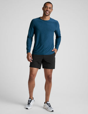 man wearing a blue long-sleeve shirt and black shorts against a gray background. 