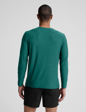 Man wearing a green long sleeve top and black shorts against a light grey background. 