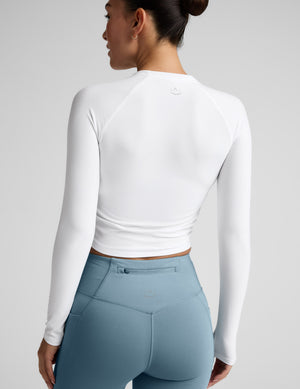 Woman wearing a white long-sleeve top and blue leggings against a gray background. 