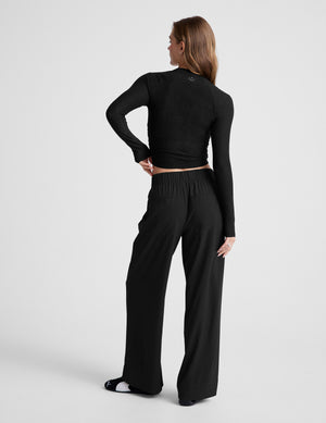 Woman wearing a black long-sleeve top and black pants on a light gray background. 