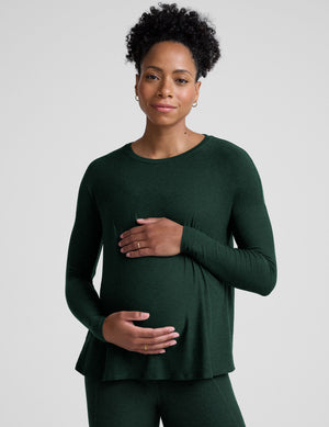 model wearing a green maternity crew neck long-sleeve top and leggings against a light gray background. 