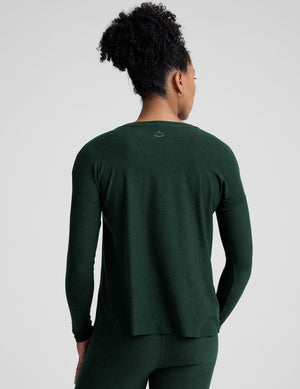 model wearing a green maternity crew neck long-sleeve top and leggings against a light gray background. 