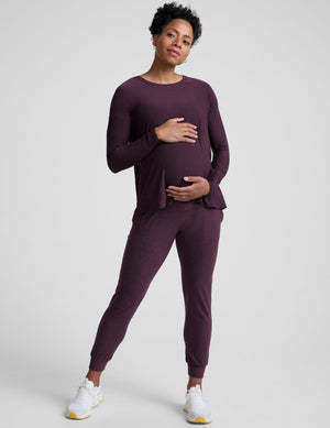 model wearing a purple maternity long sleeve crew neck top and joggers against a light gray background. 