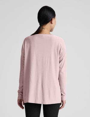 Pregnant woman wearing a pink long sleeve top and black leggings on a light gray background. 