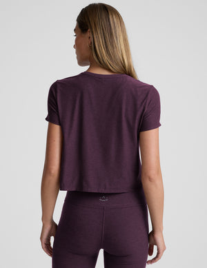 model wearing a purple cropped crew neck t-shirt and pants on a plain background. 