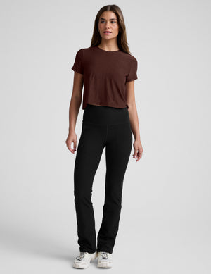 Woman wearing a brown cropped t-shirt and black bootcut pants against a plain background. 
