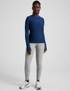 Woman wearing a blue long-sleeve top and gray leggings on a light gray background. 