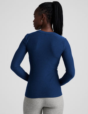 Woman wearing a blue long-sleeve top and gray leggings on a light gray background. 