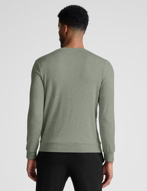 Man wearing a green long-sleeve shirt and black pants on a light gray background. 