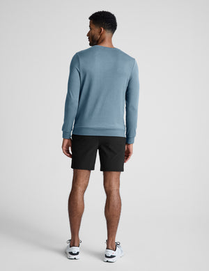 Man wearing a blue sweater and black shorts on a white background. 