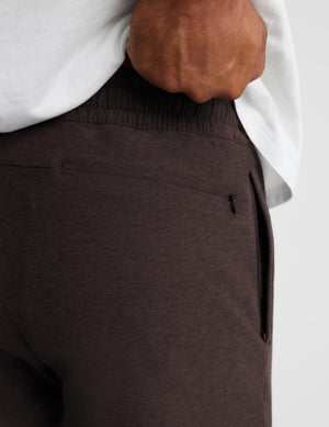 Close-up of a person wearing dark brown heathered lounge pants with an elastic waistband and side pocket, paired with a white shirt.