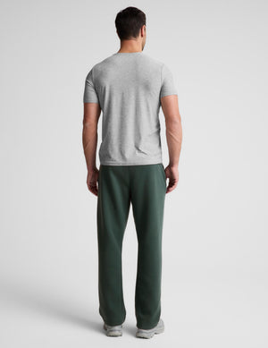 A man viewed from behind wearing a light gray short-sleeve t-shirt and dark green sweatpants against a light gray studio background.