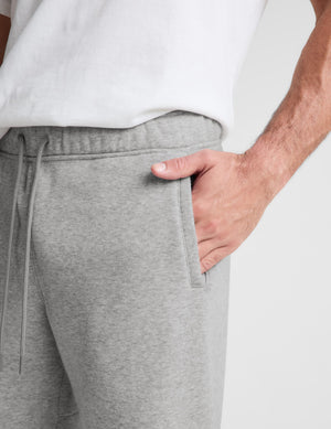 Close-up of a person wearing light heather gray sweatpants with a drawstring waist and side pocket, paired with a white top against a plain light background.