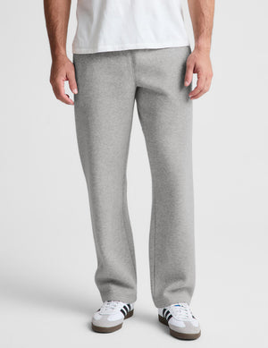 A person wearing light heather gray sweatpants with a white t-shirt and white sneakers, shown from the waist down against a light gray studio background.
