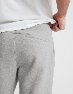 Close-up back view of a person wearing light heather gray sweatpants and pulling down a white t-shirt, showing the back pocket detail.