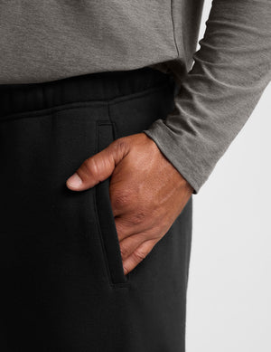 Close-up of a person wearing black sweatpants and a heather gray long-sleeve top, with the hand inserted into the side pocket of the pants.