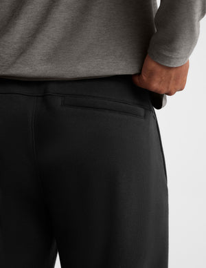 Close-up of a person wearing black sweatpants and a gray long-sleeve top, showing the back waistband and side pocket area against a light gray background.