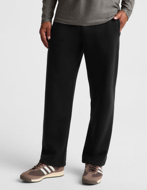 A person wearing black straight-leg sweatpants, a gray long-sleeve top, and brown sneakers, shown from the waist down against a light gray studio background.
