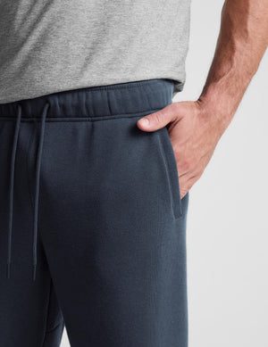 Close-up of a person wearing dark slate blue sweatpants with an elastic drawstring waistband and side pocket, paired with a heather gray t-shirt.