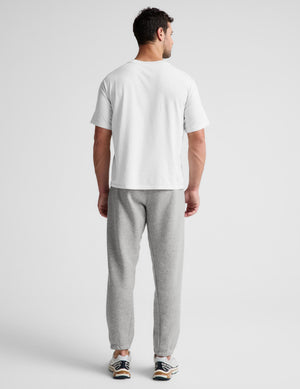 A man viewed from behind wearing a white short-sleeve t-shirt and light gray heather sweatpants, standing against a light gray studio background.