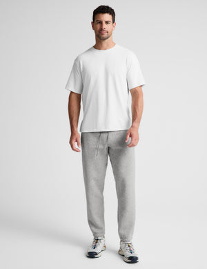 A man modeling a white short-sleeve crewneck t-shirt and light gray sweatpants against a light gray studio background.