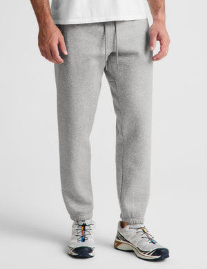 A person wearing light heather gray jogger sweatpants with a drawstring waist and elastic cuffs, paired with white sneakers, shown from the waist down on a light gray studio background.