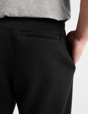 Close-up of a person wearing black sweatpants with a side pocket and a gray heather t-shirt, showing the back waistband and hand in pocket.