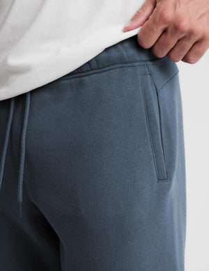 Close-up of a person wearing dark slate blue sweatpants with a drawstring waist and a side pocket, paired with a white top.