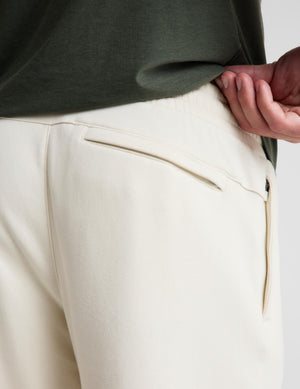 Close-up of a person wearing cream-colored trousers with a zippered pocket and a dark olive green top, showing the waistband and side pocket detail.