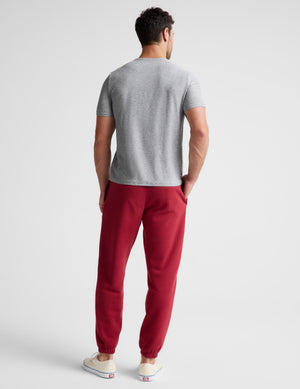 A man viewed from behind wearing a light gray short-sleeve t-shirt and red jogger pants, standing against a light gray studio background.