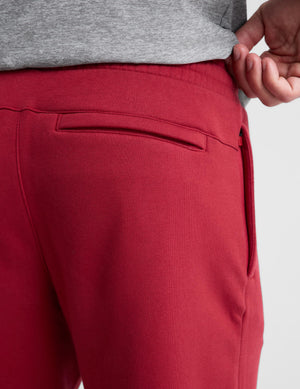 Close-up of a person wearing red sweatpants, showing the back pocket, waistband, and a hand pulling up a gray sweatshirt.