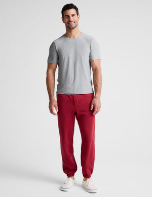 A man modeling a light gray crewneck t-shirt and red jogger sweatpants against a light gray studio background.