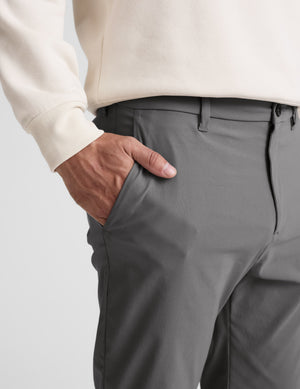 Person wearing gray pants and a white sweater on a light gray background. 