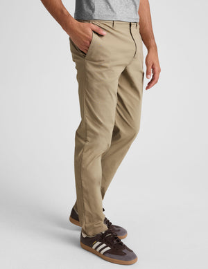 man wearing beige chino pants with side pockets on a plain background. 