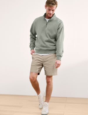 Man wearing a green sweater and beige shorts against a plain background. 