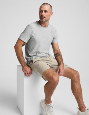 Man wearing a gray shirt and beige shorts against a plain background. 