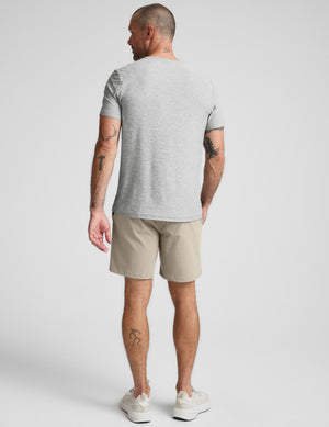 Man wearing a gray shirt and beige shorts against a plain background. 