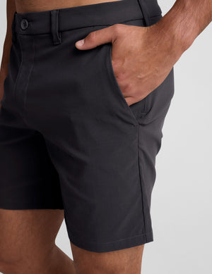man wearing a grey crew neck t-shirt and black chino shorts with pockets on a plain background. 