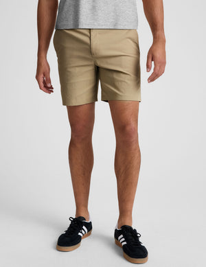 man wearing a grey crew neck t-shirt and beige chino shorts with pockets standing against a plain background. 