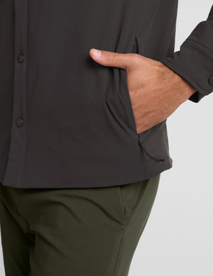 Man wearing a dark jacket, black shirt, green pants, and black sneakers on a white background