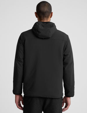 male model wearing a black zip-up jacket with a hood and pockets against a plain background. 