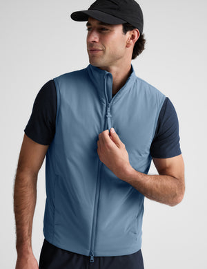 Man wearing a light blue vest over a black shirt on a plain background. 