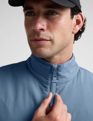 Man wearing a light blue vest over a black shirt on a plain background. 