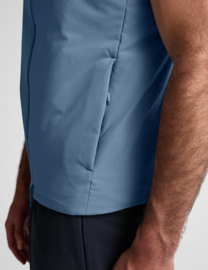 Man wearing a light blue vest over a black shirt on a plain background. 