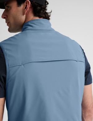 Man wearing a light blue vest over a black shirt on a plain background. 